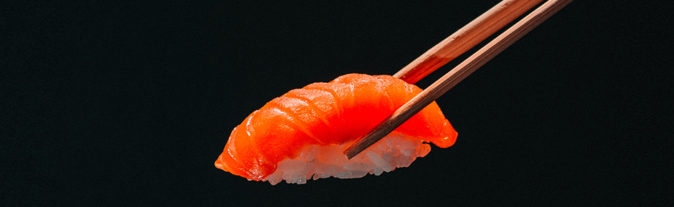 Image décorative / un sushi saumon tenu par des bagettes en bois