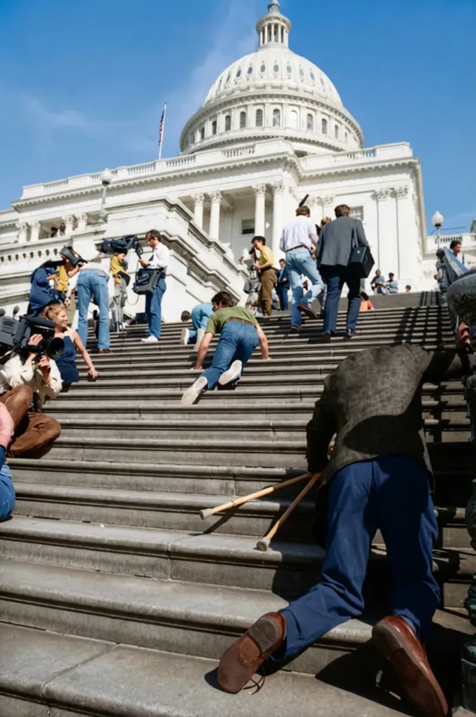 Des personnes handicapées montent les marches du Capitole à genoux, laissant leur fauteuil et béquilles en bas des marches